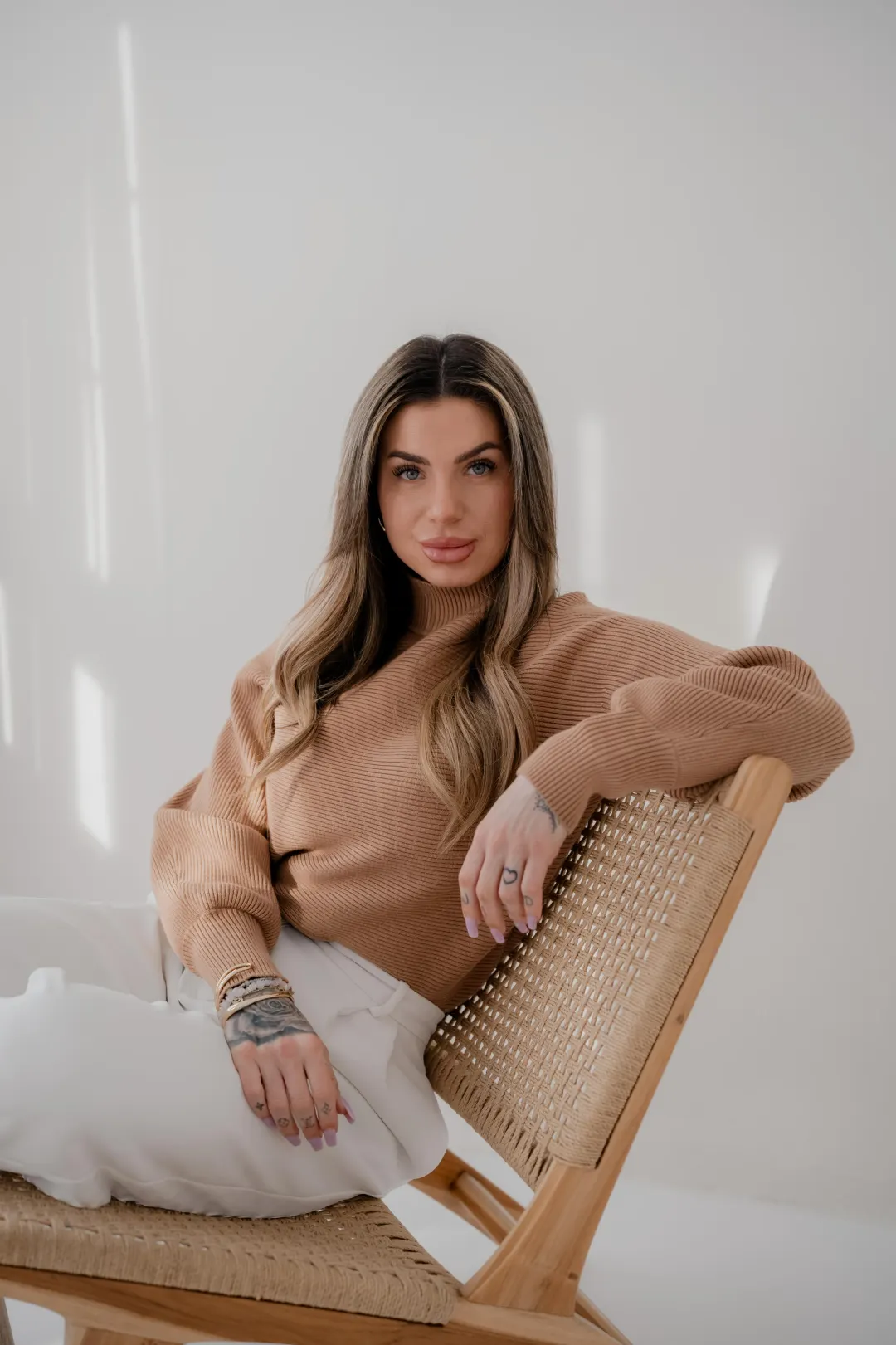 Emily Klatt im sandfarbenen Pullover auf einem Rattanstuhl, mit offenem Blick
